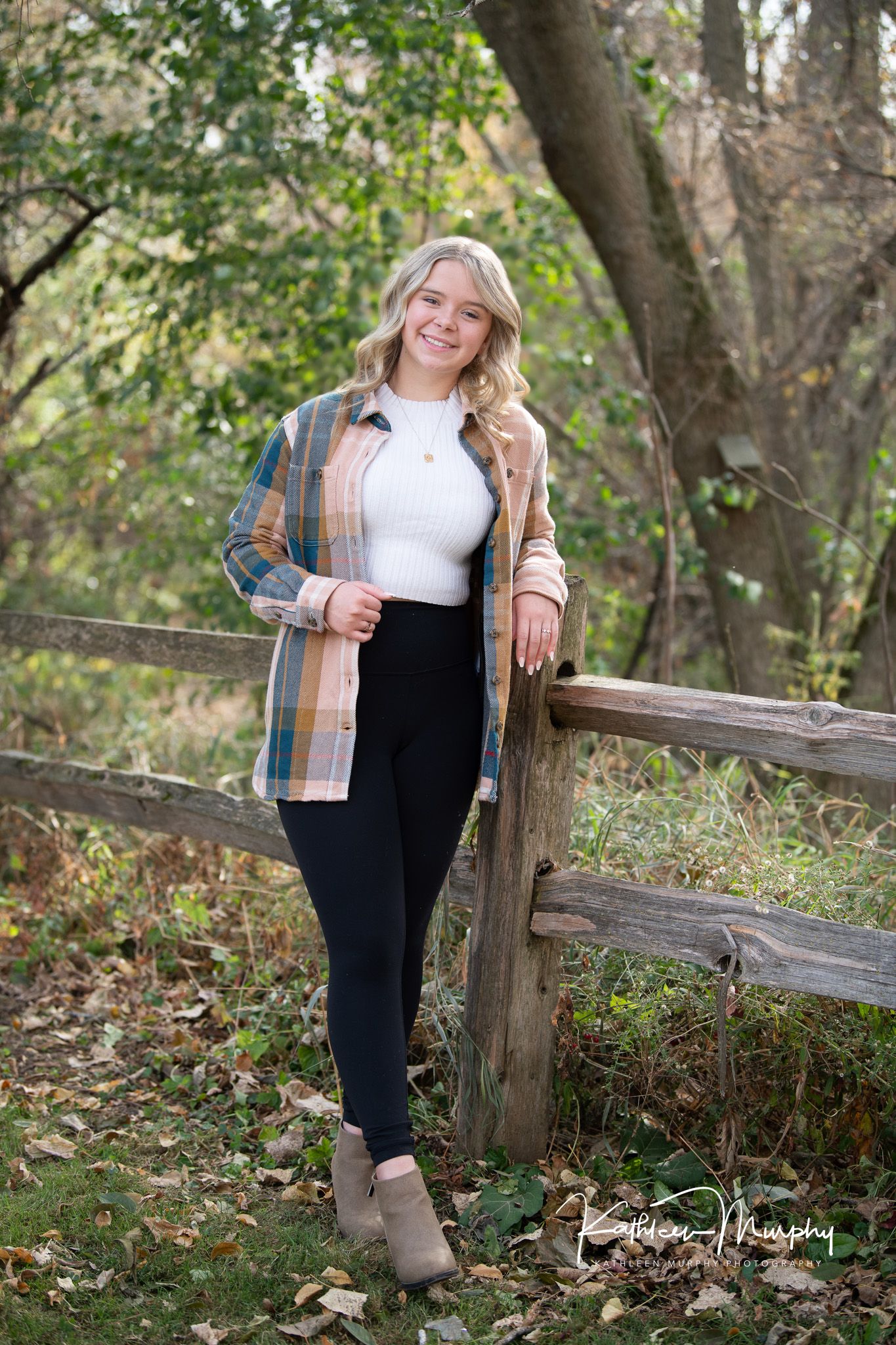 Casual autumn fashion look with plaid shirt and ankle boots against rustic wooden fence in fall setting.
