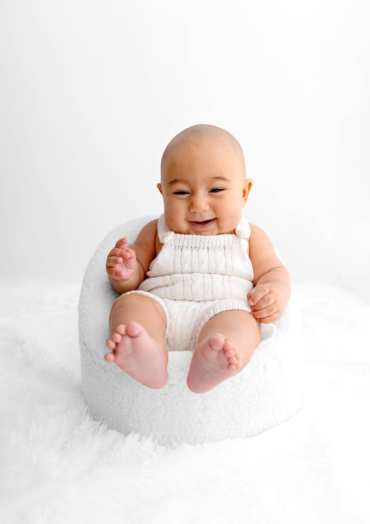 Smiling infant wearing white romper sitting in round white chair.