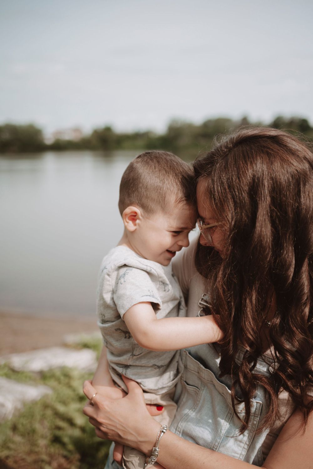 A tender moment shared between parent and child by a lakeside on a bright day.