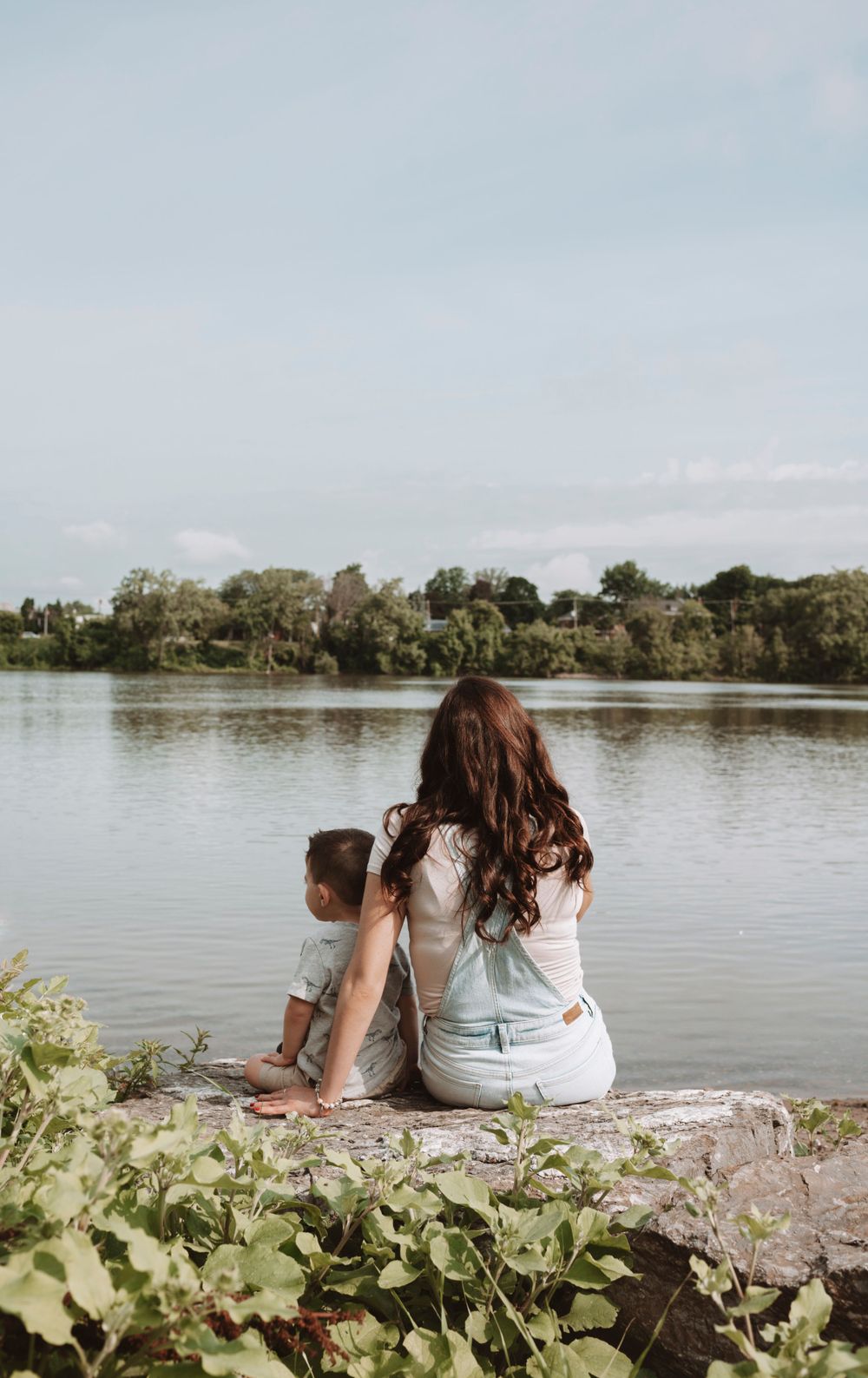 Family sitting together on rocks by a peaceful lake surrounded by green vegetation.