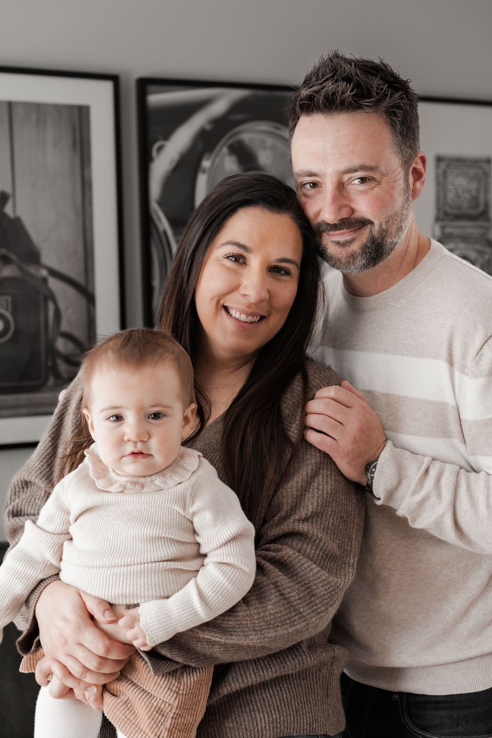 A cozy indoor family portrait featuring warm neutral colors and matching outfits.