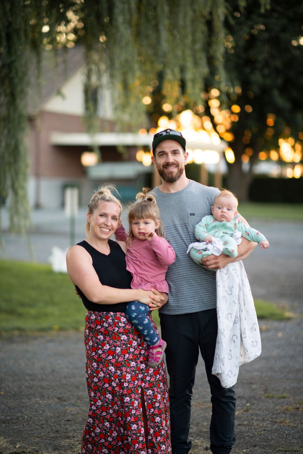 A family portrait under a weeping willow tree at sunset with parents holding small children.