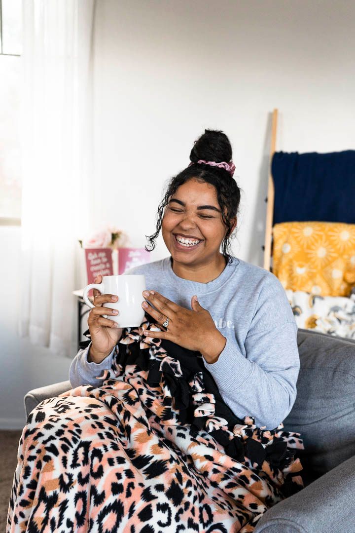Business owner laughing drinking coffee snuggling a handmade blanket in a cozy chair in phoenix arizona