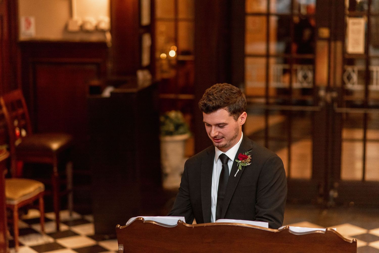 A speaker stands at a wooden podium reading from papers during what appears to be a wedding ceremony.