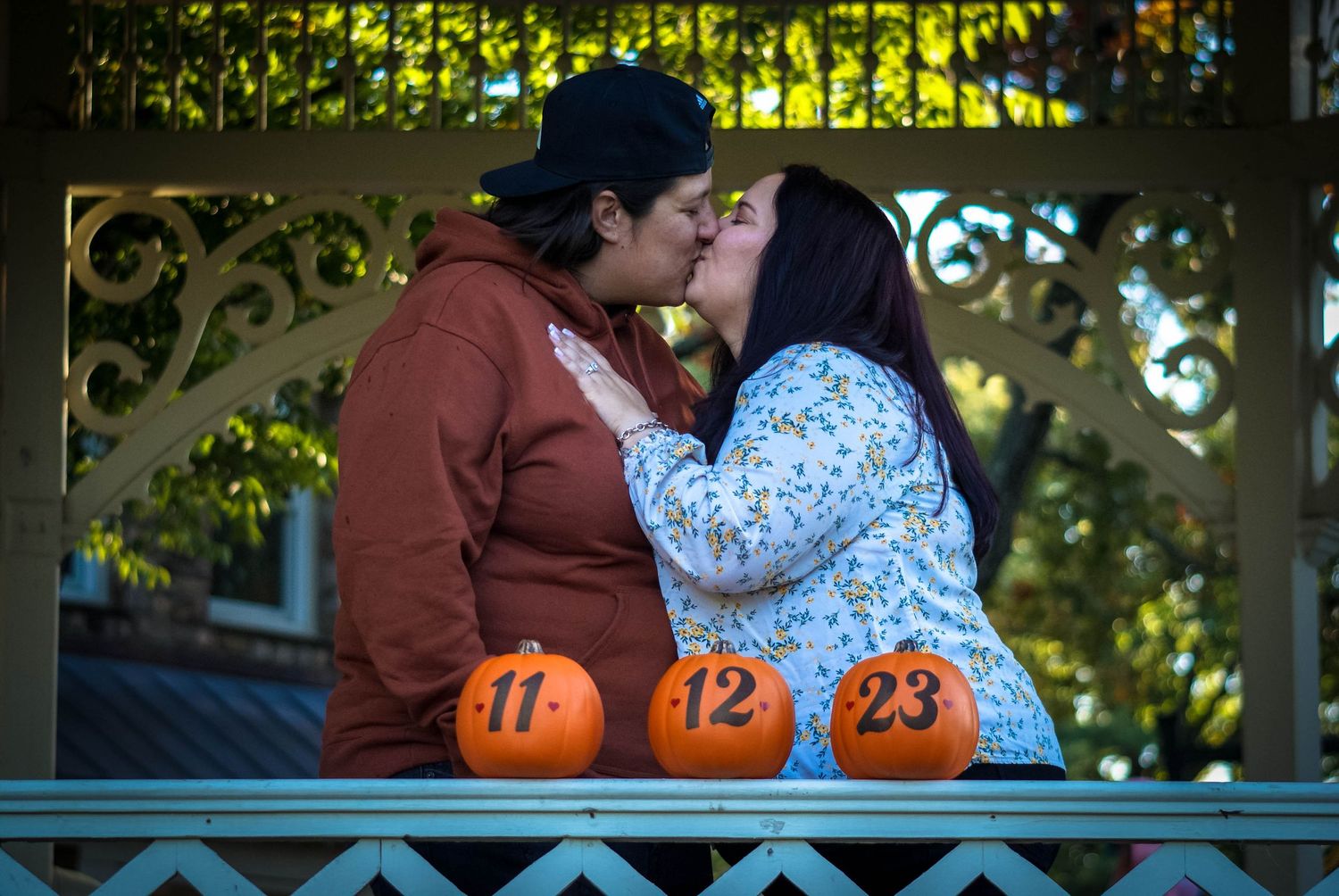Couple shares an intimate moment next to numbered autumn pumpkins on a porch.