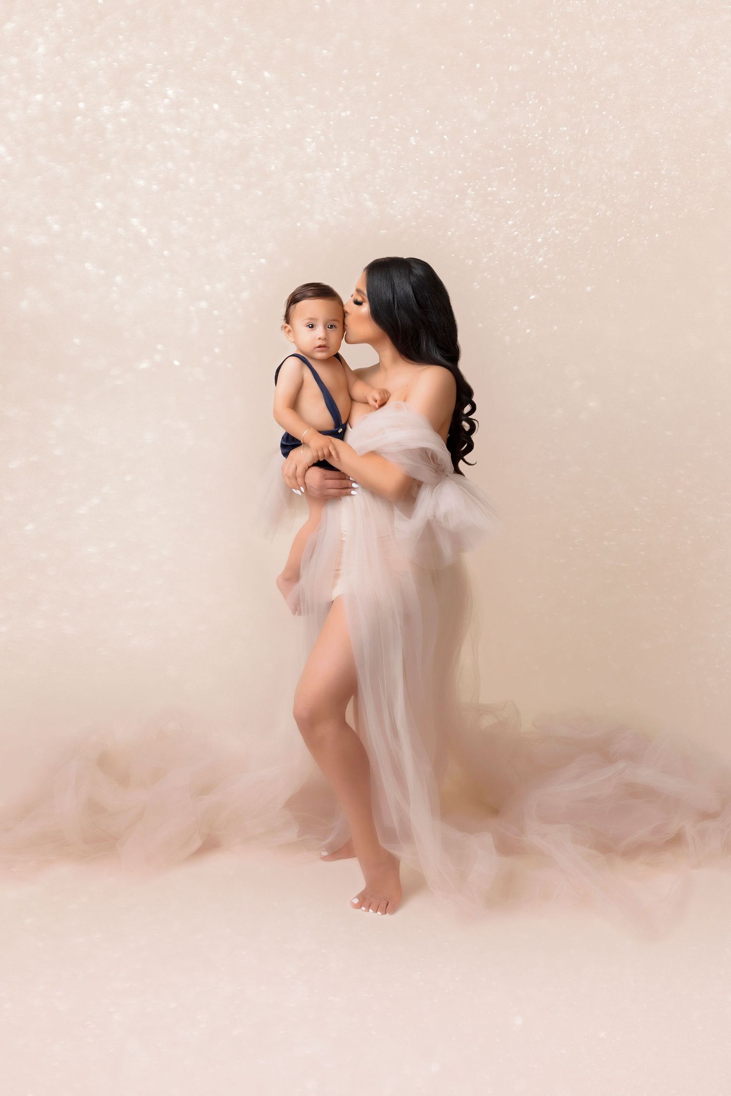 Mother and child in ethereal white dresses against beige background with sparkle effects.