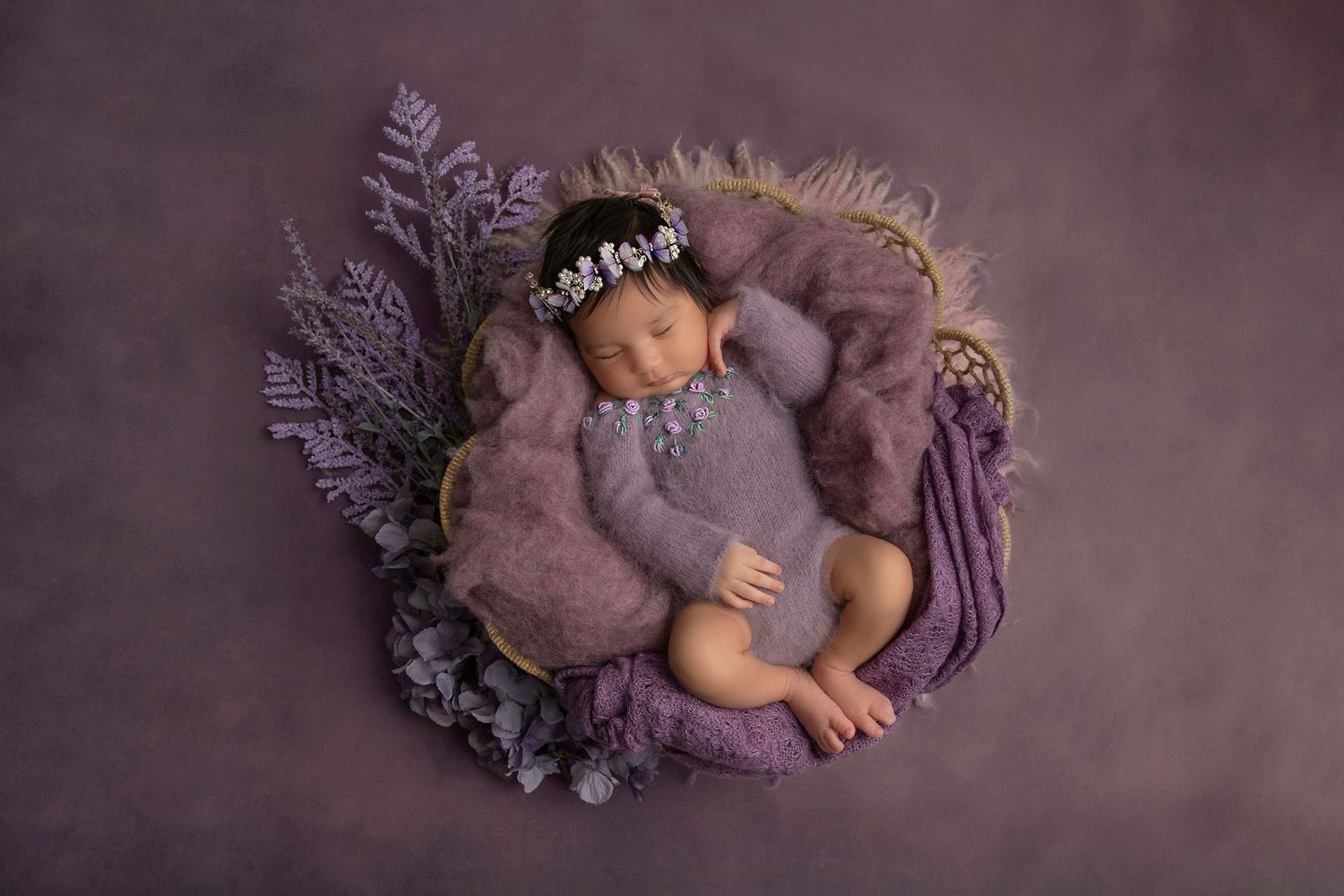 Sleeping baby nestled in purple and grey decor with floral accents.