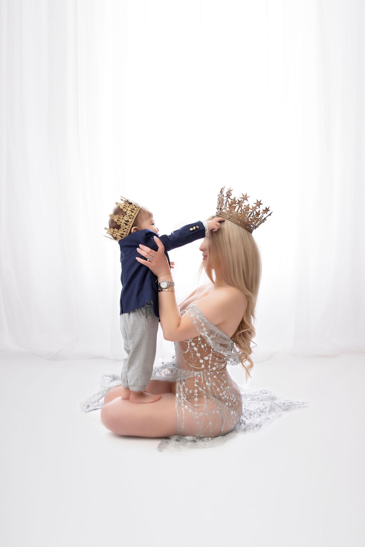 Studio portrait with sparkly dress and gold crowns against white backdrop.