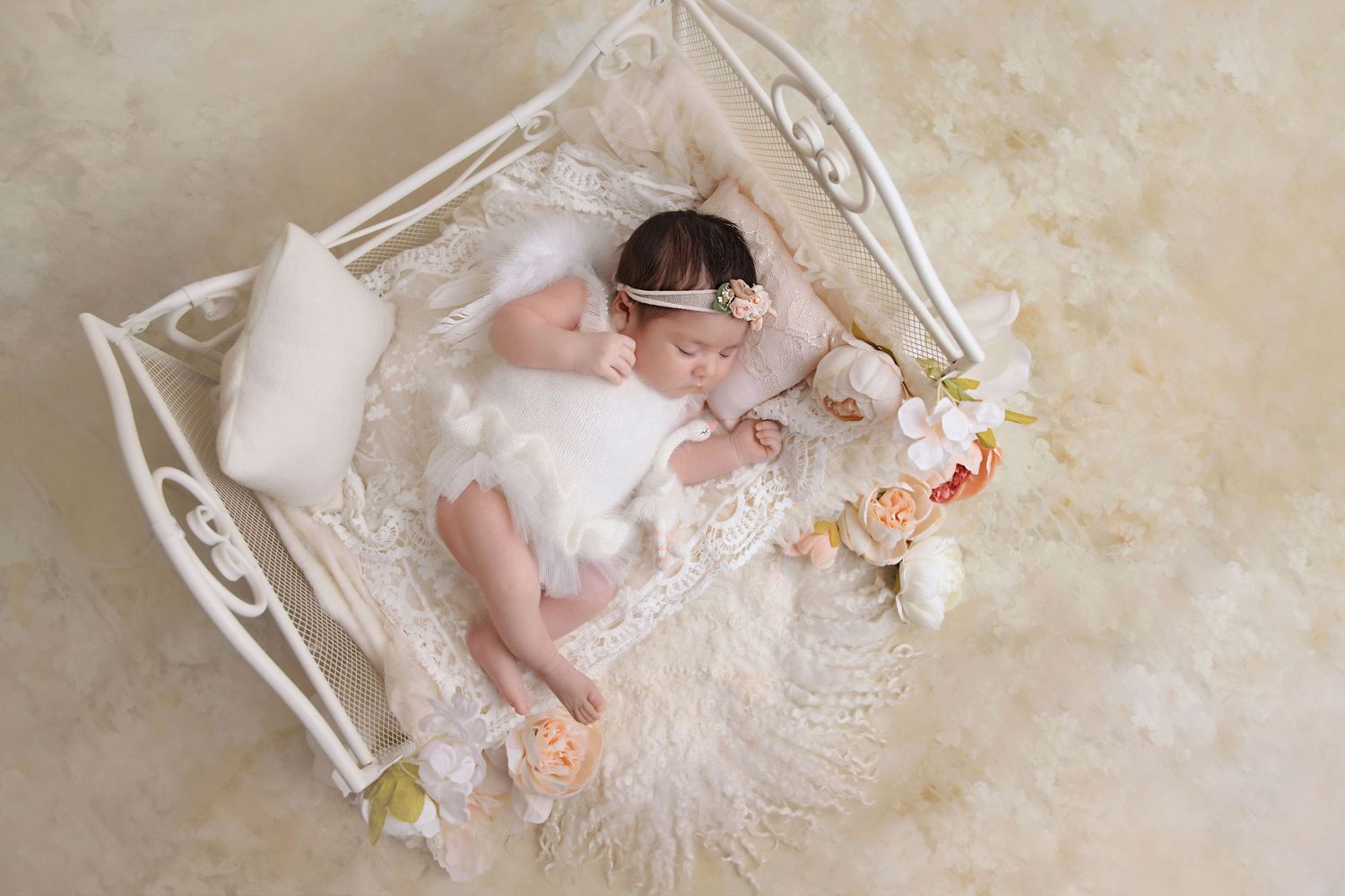 Newborn baby lies in ornate white metal bassinet with delicate lace and floral details.