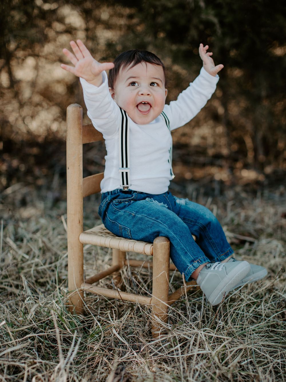 Joyful toddler in white shirt and jeans playing on wooden chair outdoors.