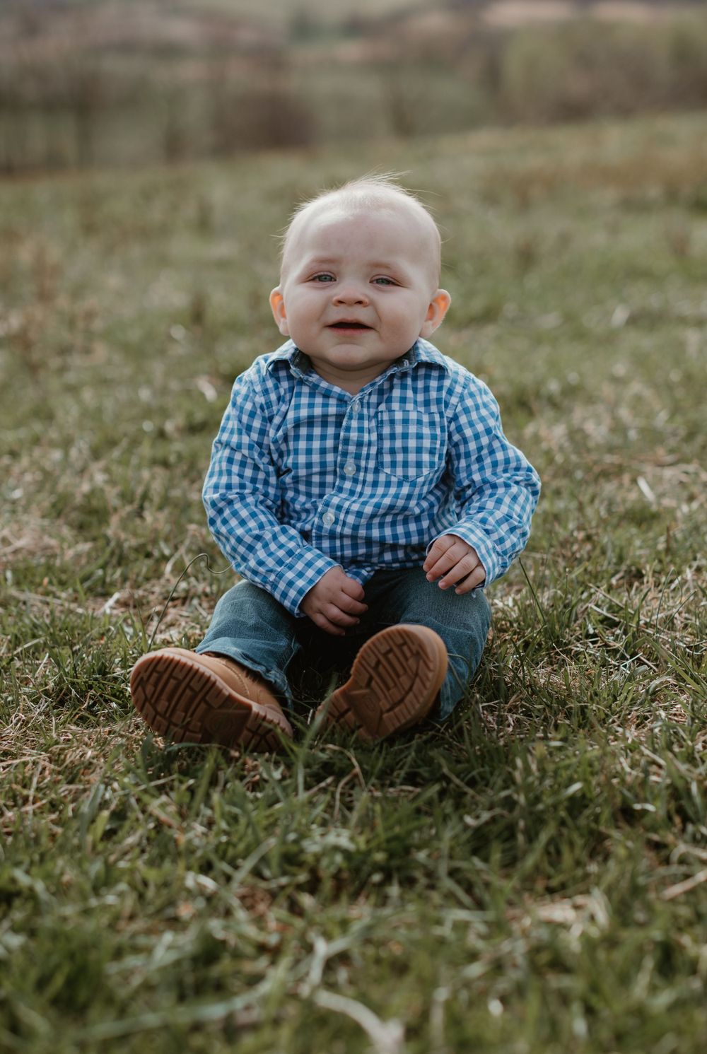 Baby wearing blue gingham shirt and jeans sits on grass in a series of candid outdoor photos.