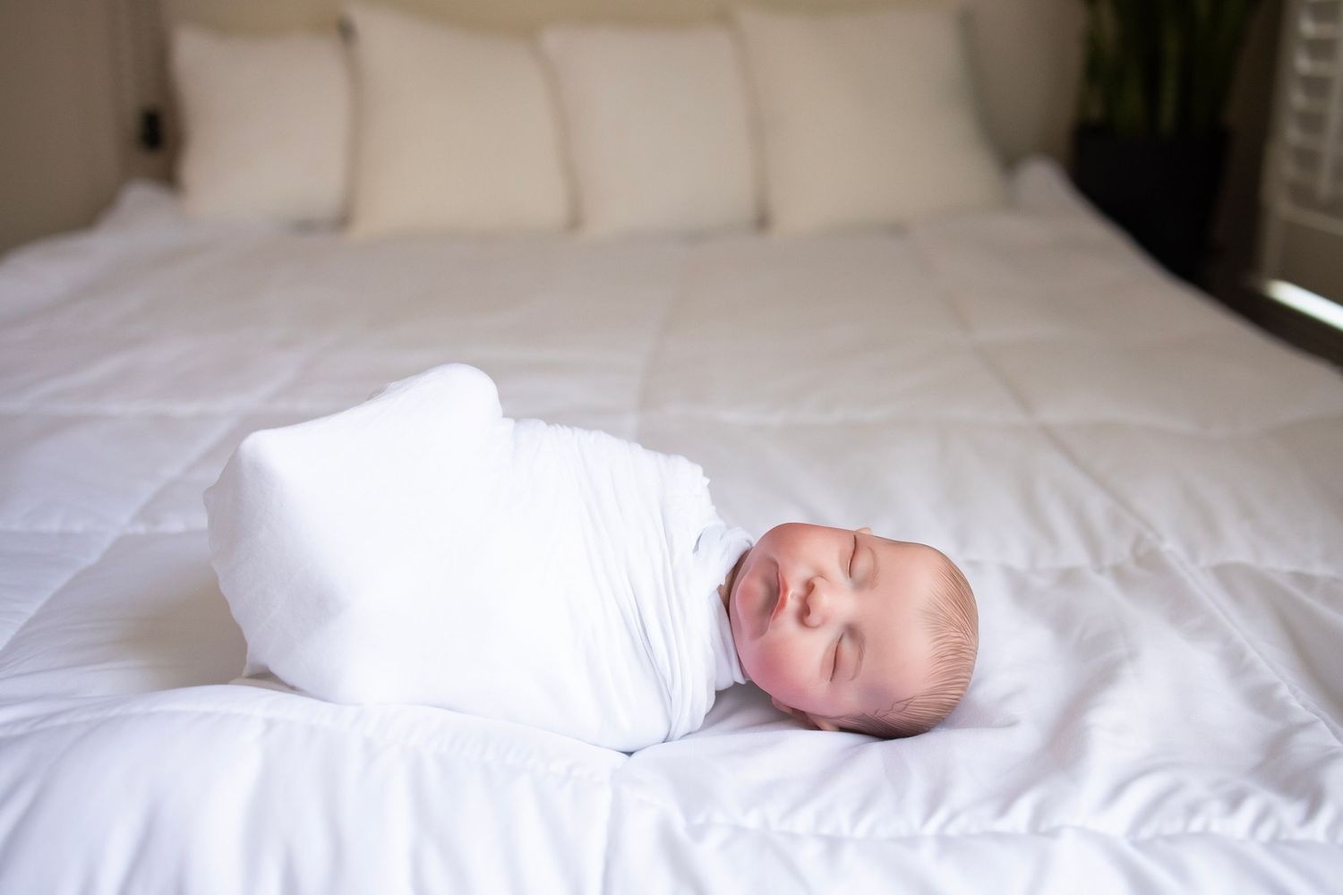 Baby doll laying on bed with white blanket and white swaddle wrap.