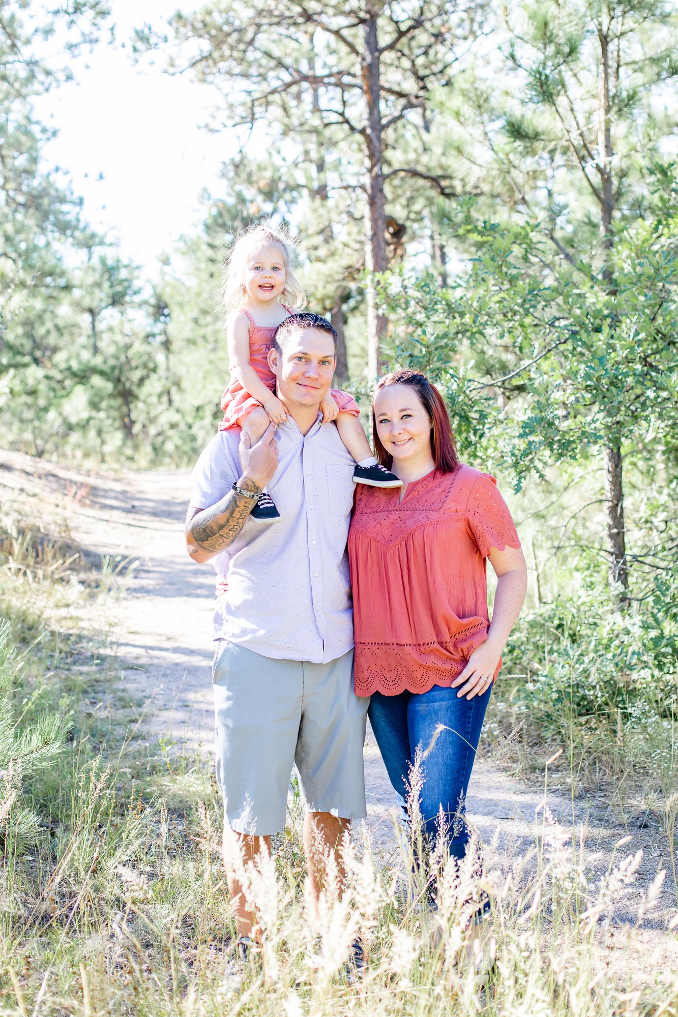 Dad carries toddler daughter on his shoulders and mom snuggles up to them on a trail in Black Forest, Colorado.