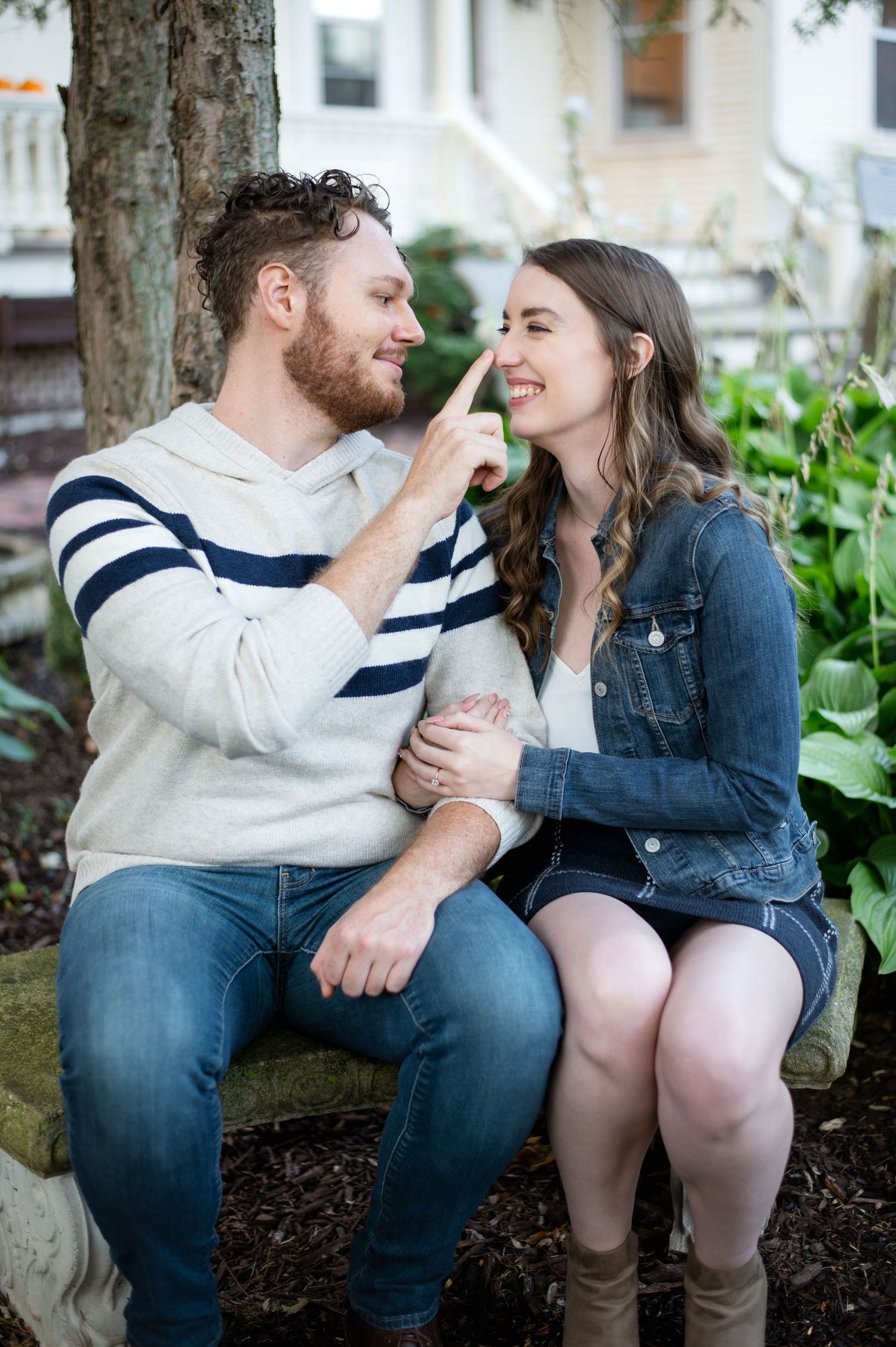 A couple sharing a playful moment while sitting together on a stone wall near greenery.
