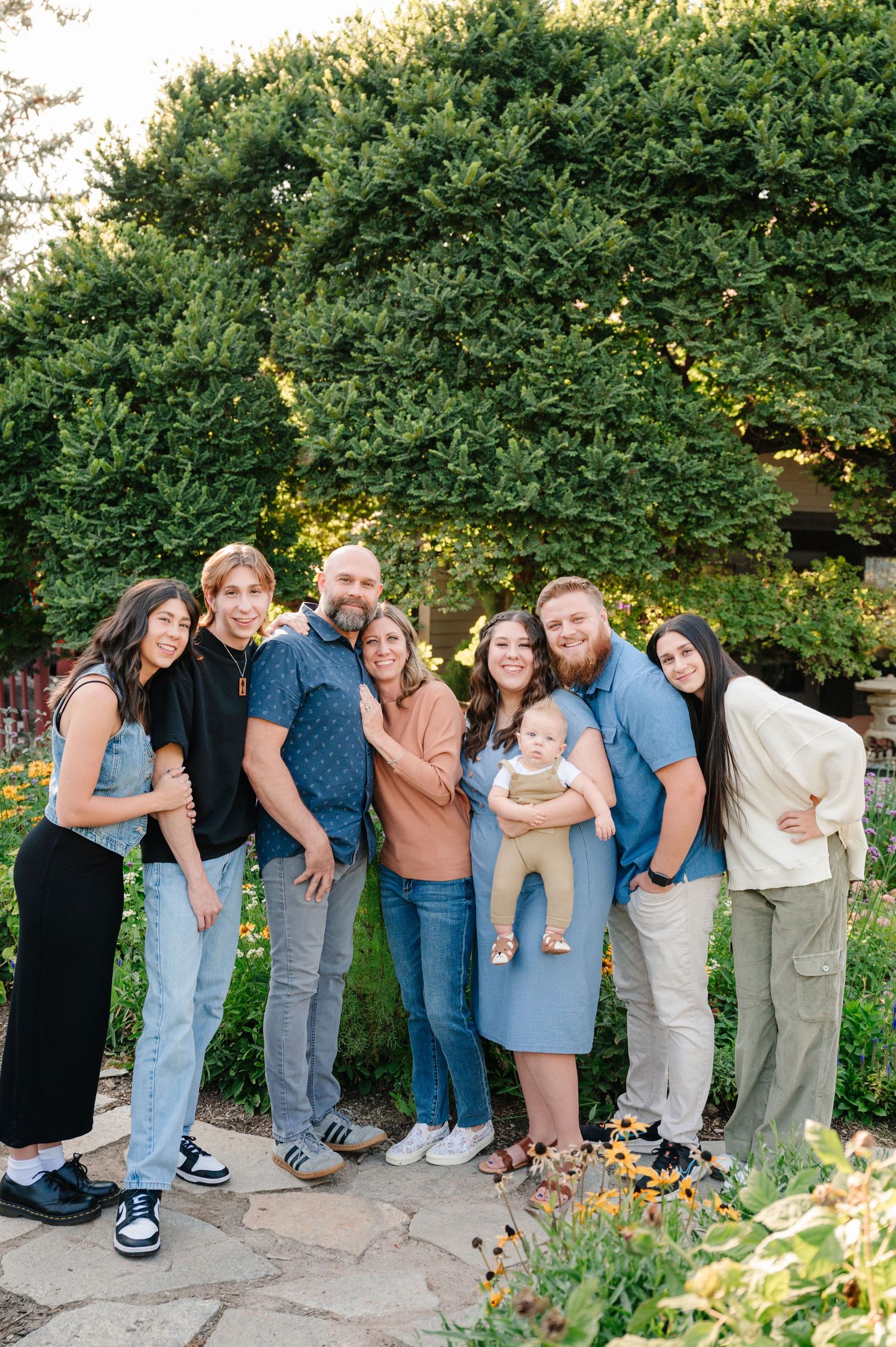 A group portrait in casual attire gathered together in front of lush garden greenery.