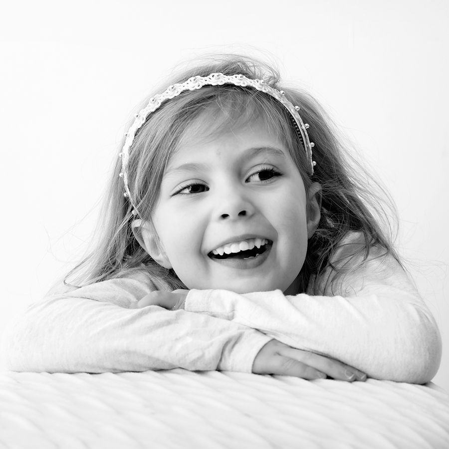 Black and white close-up of a child with a lace headband expressing joy.