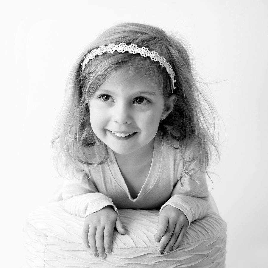 Black and white portrait of a young child wearing a lace headband and lying on white fabric.