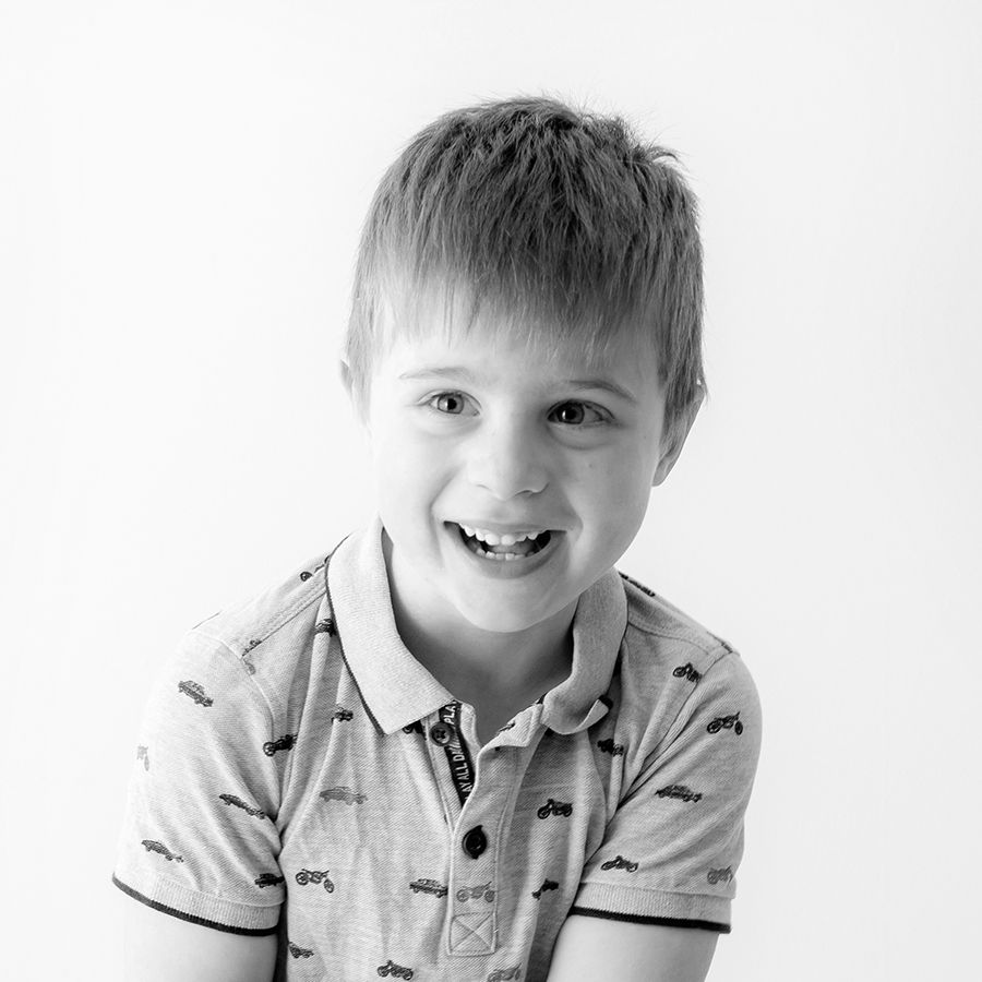 Candid black and white portrait of young child smiling in casual polo shirt.