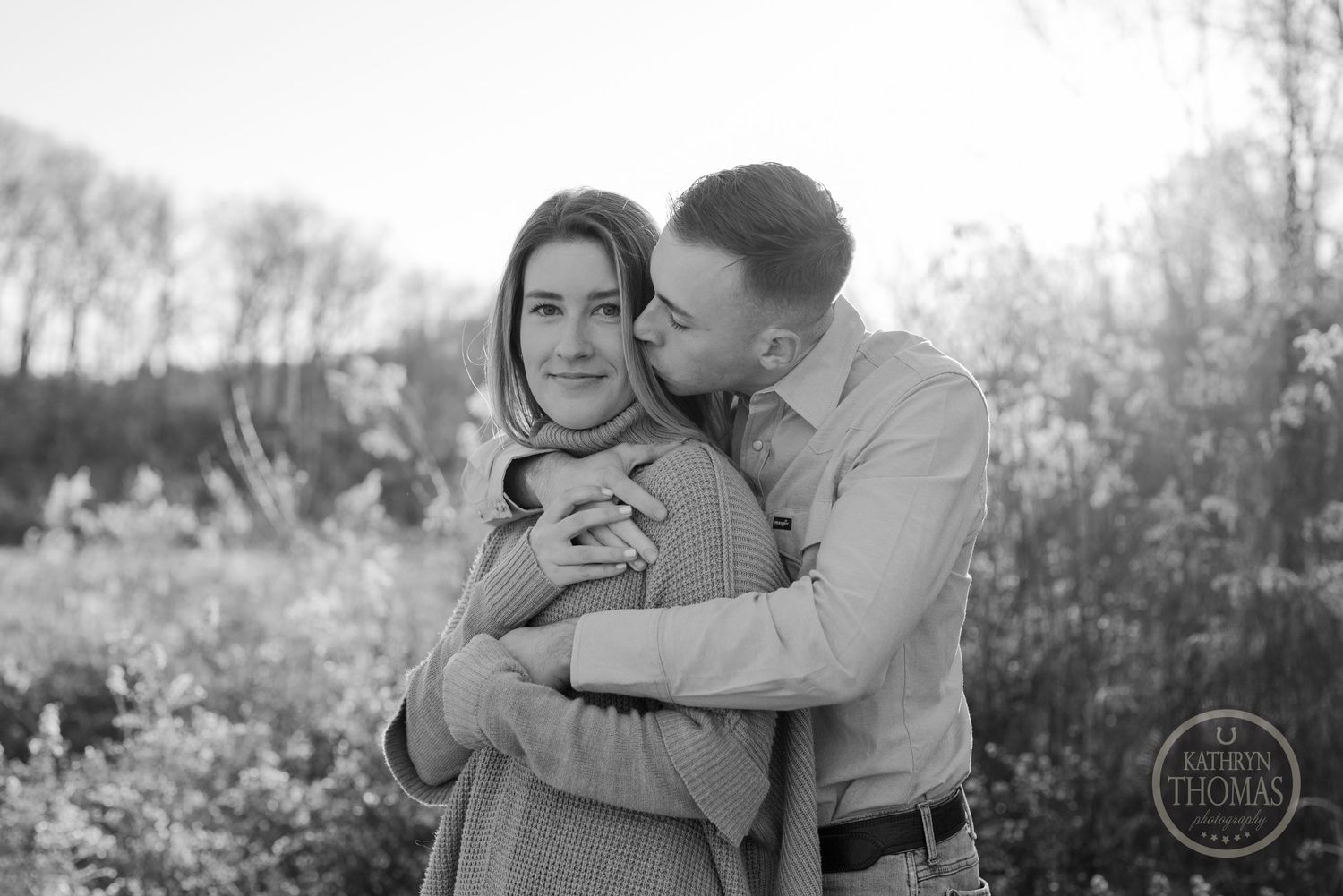 Black and white portrait of a couple sharing an affectionate embrace outdoors.