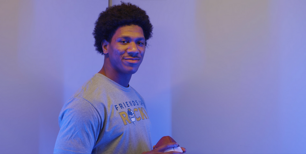 Athletic person wearing a blue shirt photographed against a purple-lit background.