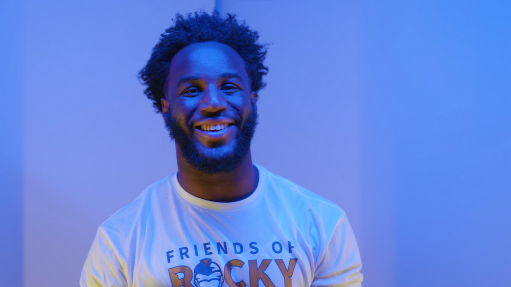 Person in a white branded t-shirt smiling against a blue-lit backdrop.