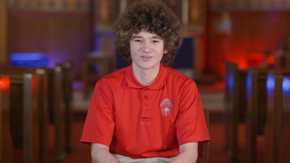 Student in red polo shirt seated in an auditorium-style setting.