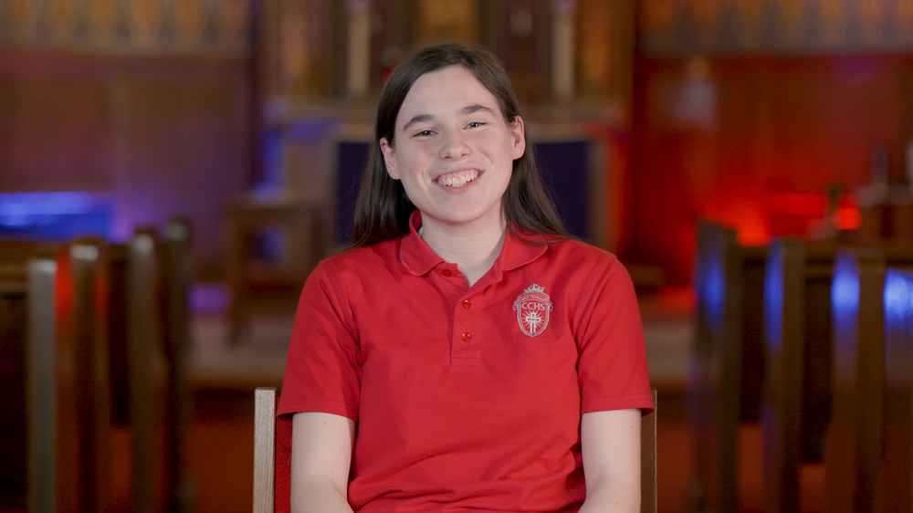 Student wearing red uniform polo shirt seated indoors.