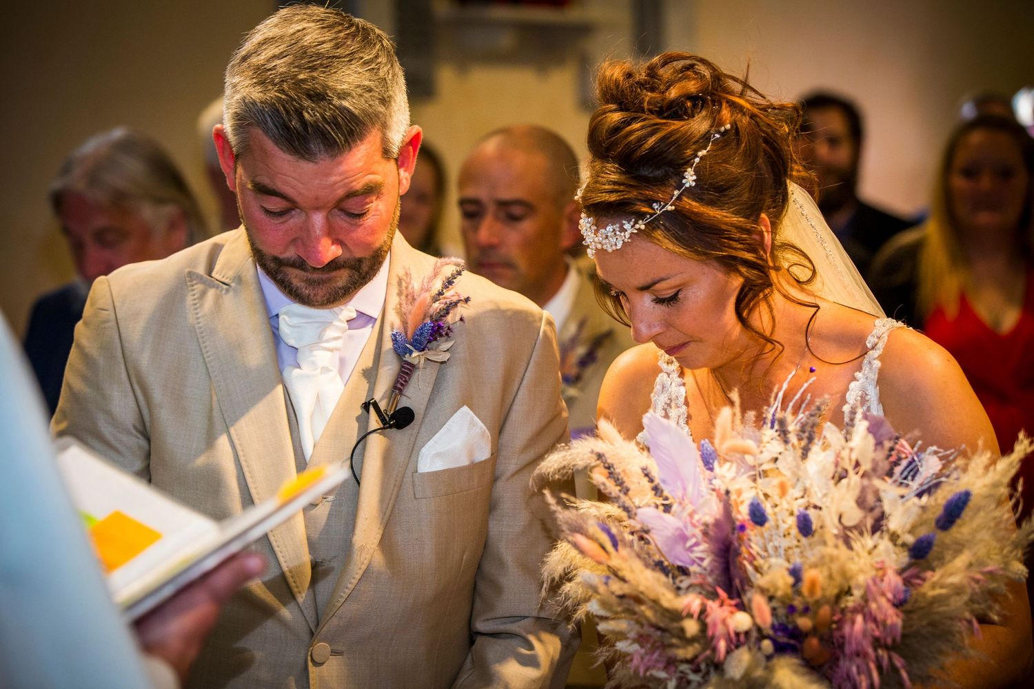 Wedding ceremony guests watch attentively by candlelight in a traditional church setting.
