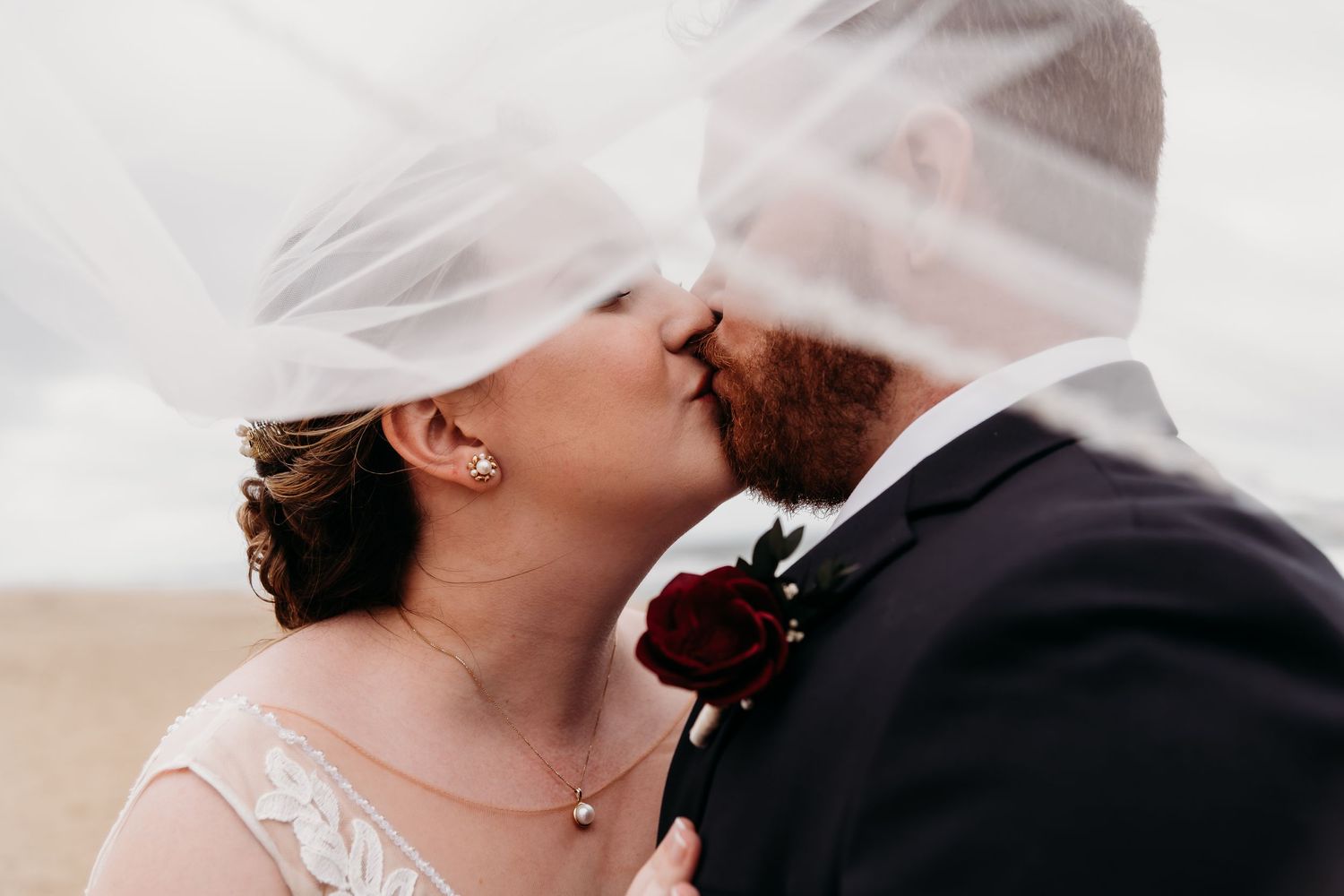 Romantic wedding kiss under flowing white veil.