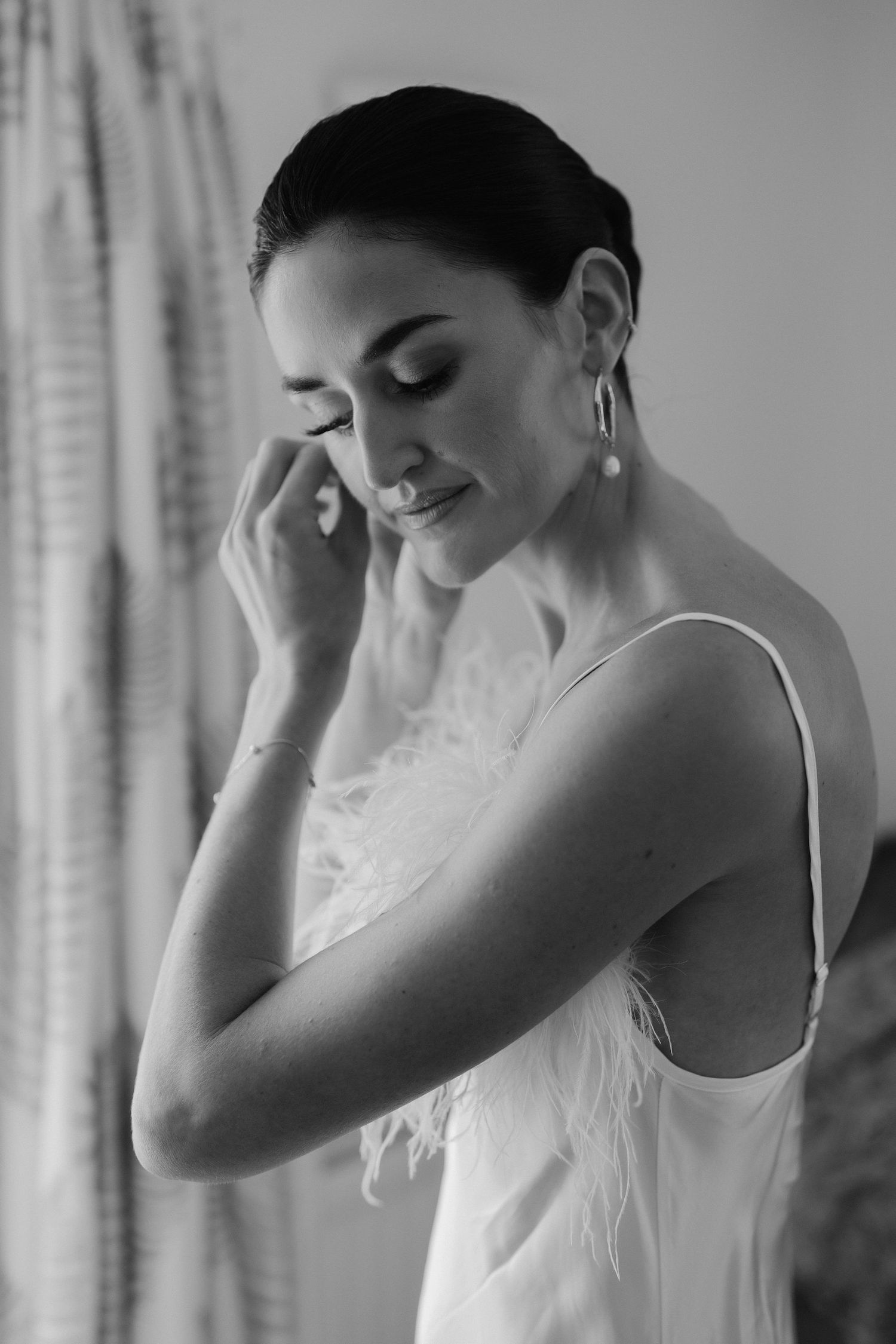 bride fastening earrings before she gets in her wedding dress in Oxfordshire