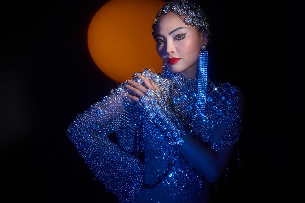 Artistic portrait in sparkling blue sequined outfit against orange backdrop.