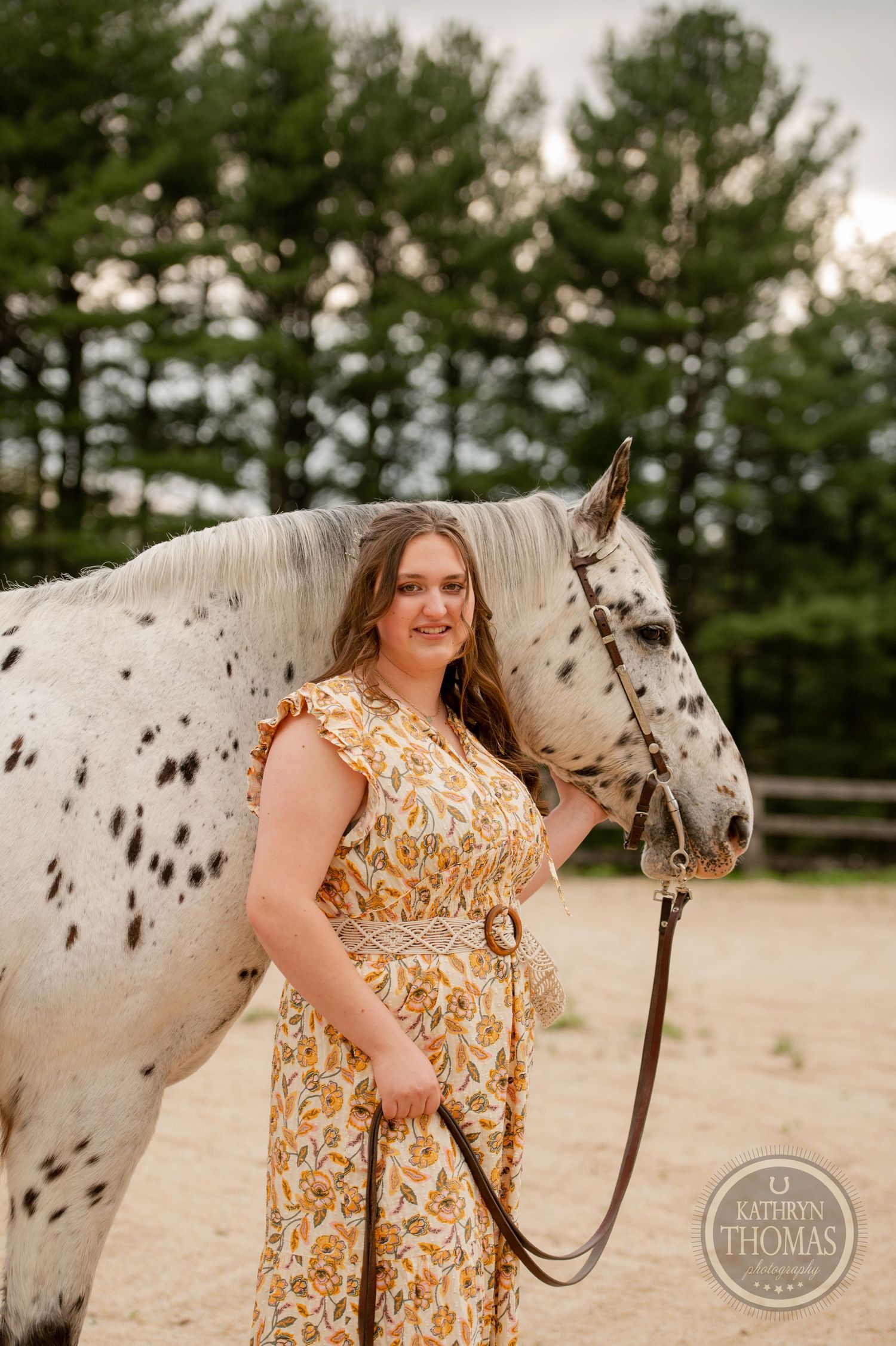 A beautiful spotted horse with dark markings stands beside someone in a floral dress.