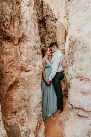 Romantic couple poses against textured rock formations during an engagement photo session.