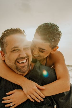 Candid moment of couple laughing and embracing in warm sunlight.