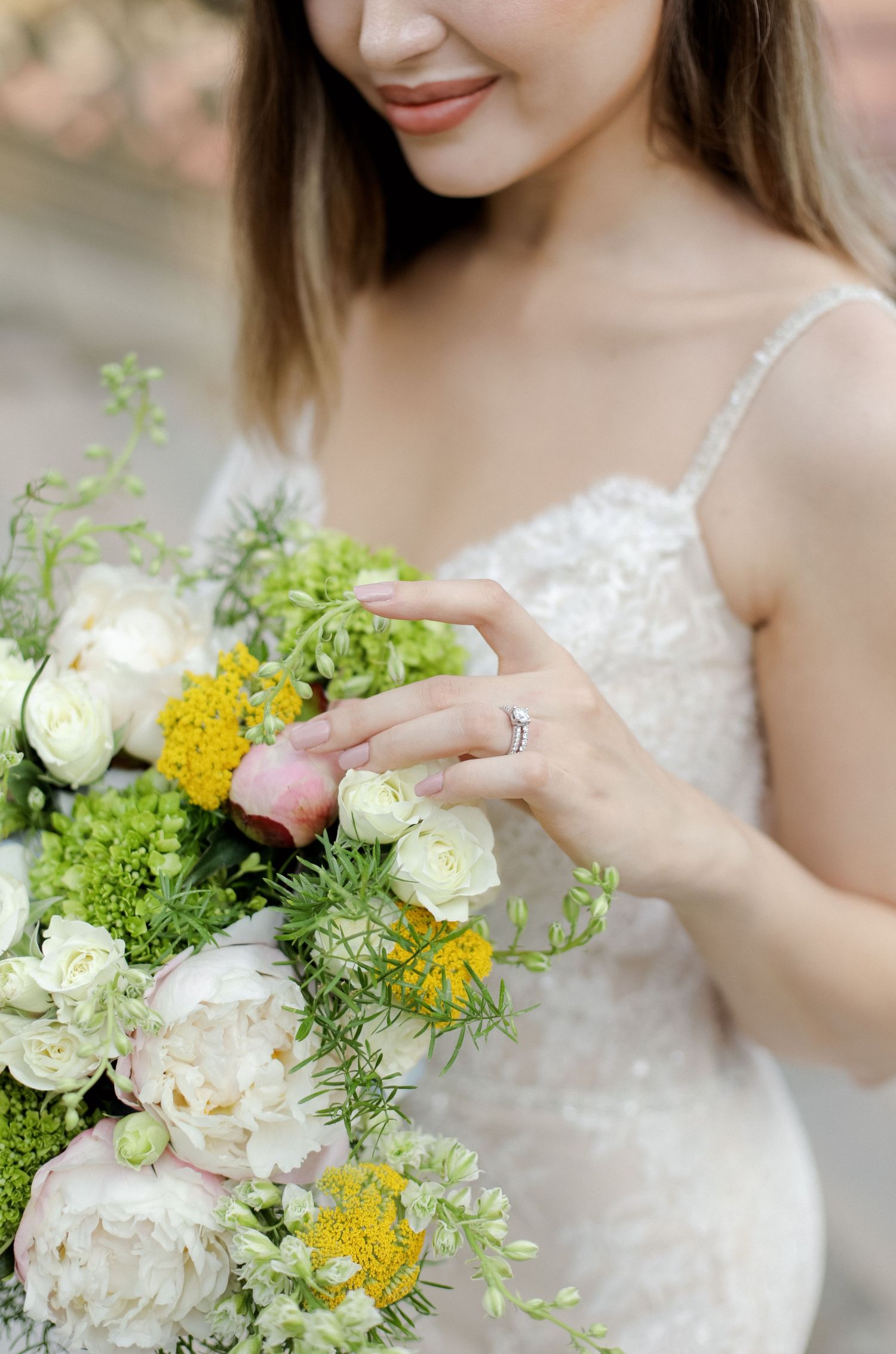 Close-up of a bridal bouquet with white peonies and yellow wildflowers with engagement ring detail.