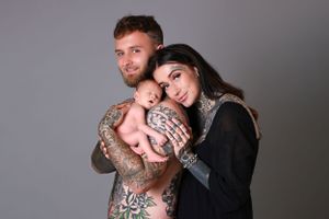 tattooed parents posed with sleeping newborn baby boy against grey backdrop at studio of photoshoot