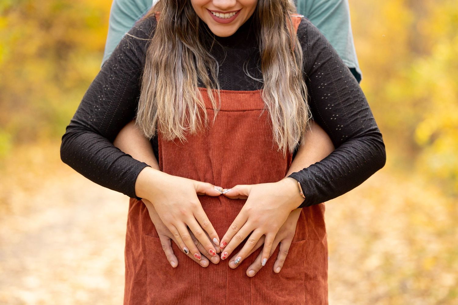 Girl in red jumper holding her stomach during a fall maternity session