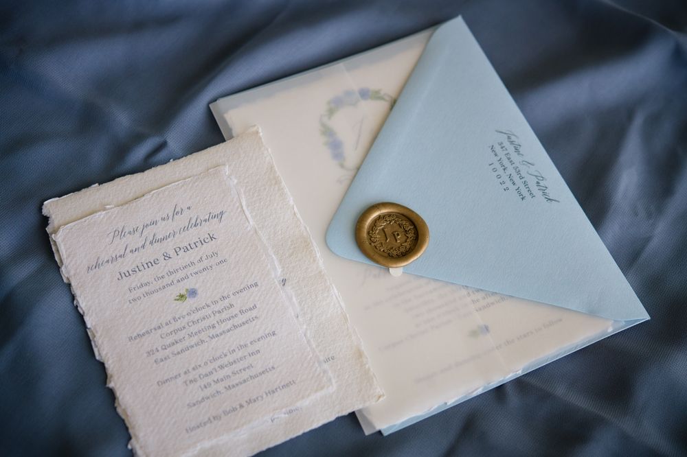Elegant wedding stationery set with wax seal and blue envelopes on dark fabric.