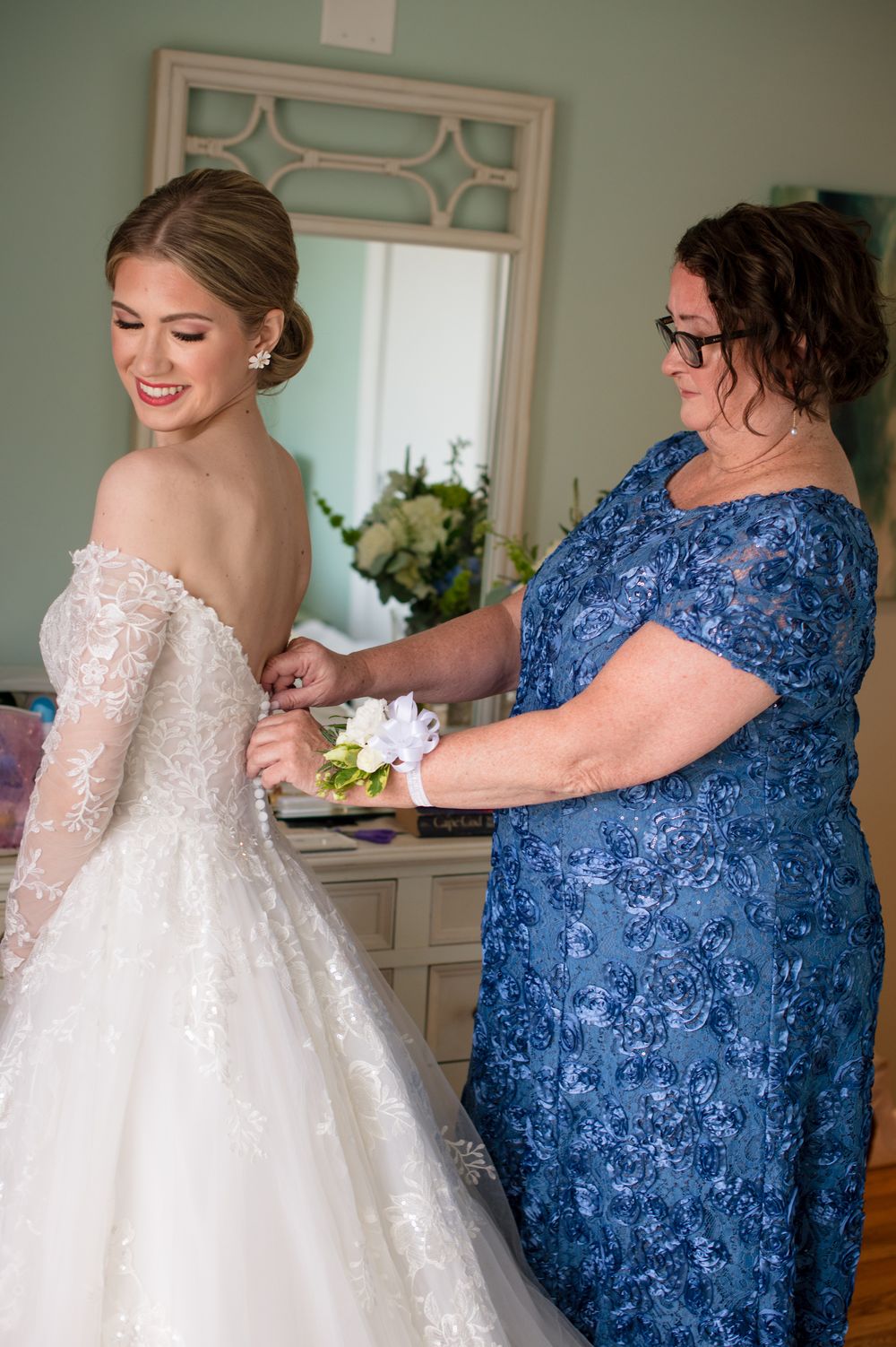 Person in blue lace dress helping with white wedding gown preparations.