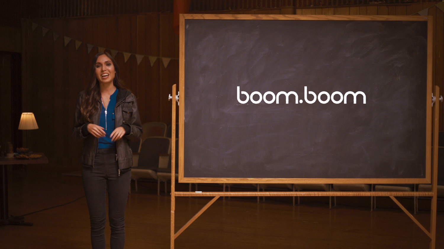 Person stands in front of a chalkboard with 'boom.boom' written on it.