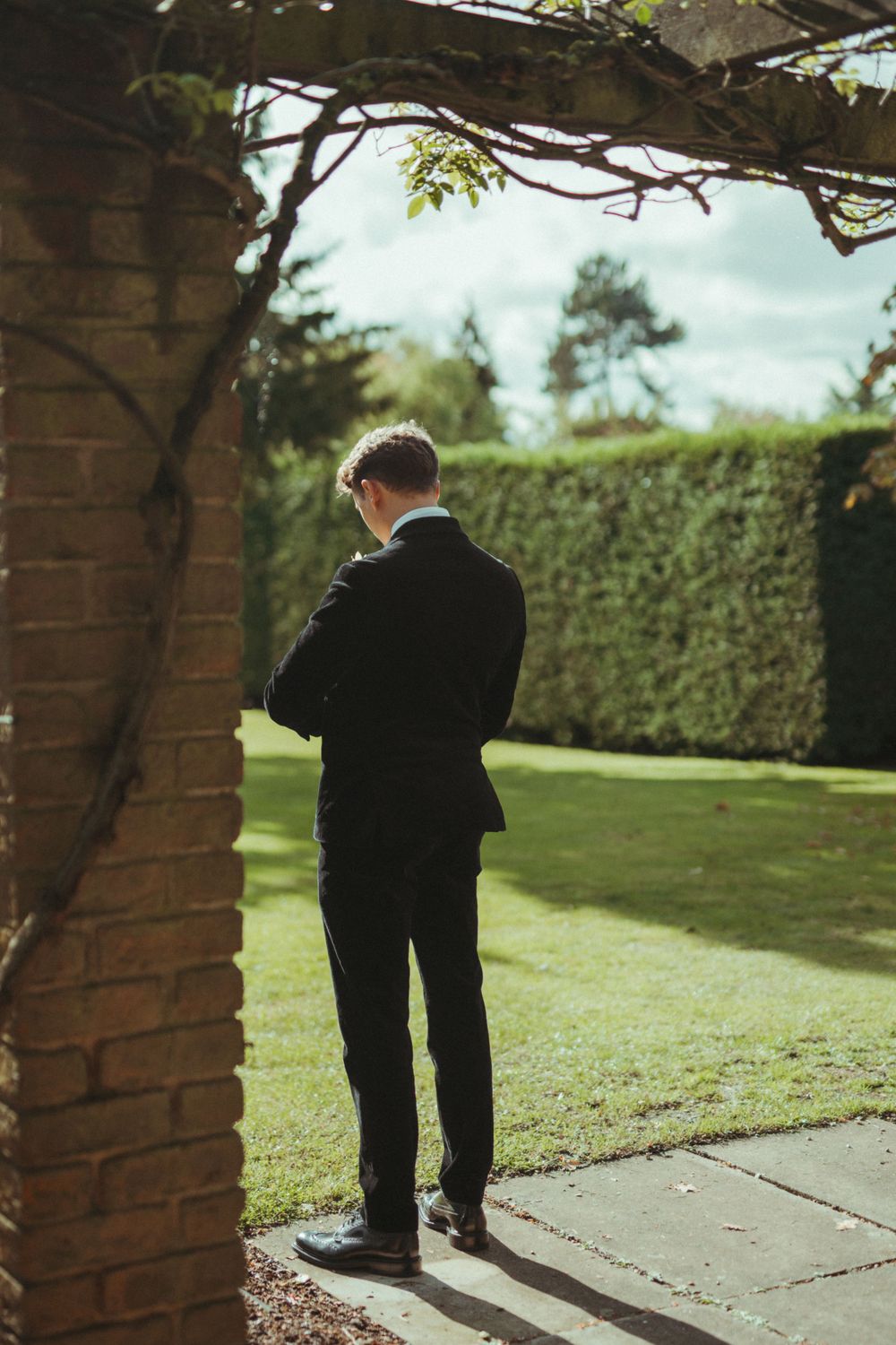 Silhouette of person in formal suit standing in garden archway. London Wedding.