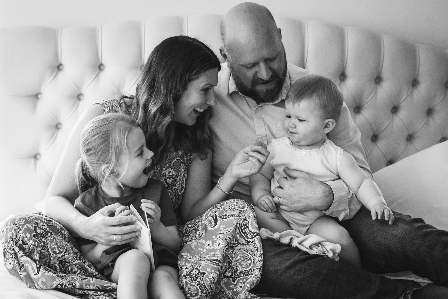An intimate black and white family portrait on a tufted couch showing tender interaction.