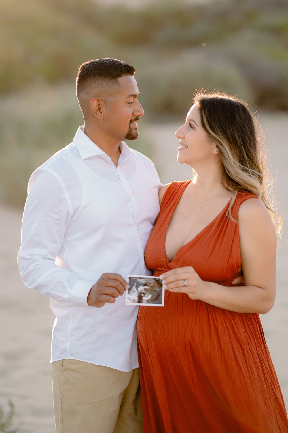 Expectant couple holds ultrasound photo during sunset maternity photoshoot.