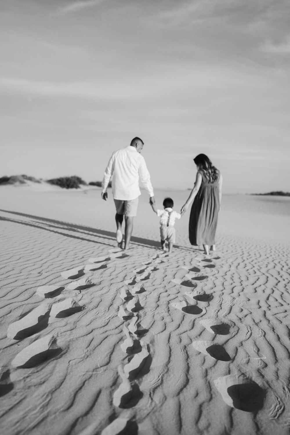 Family walking together leaving footprints in sand dunes during golden hour.