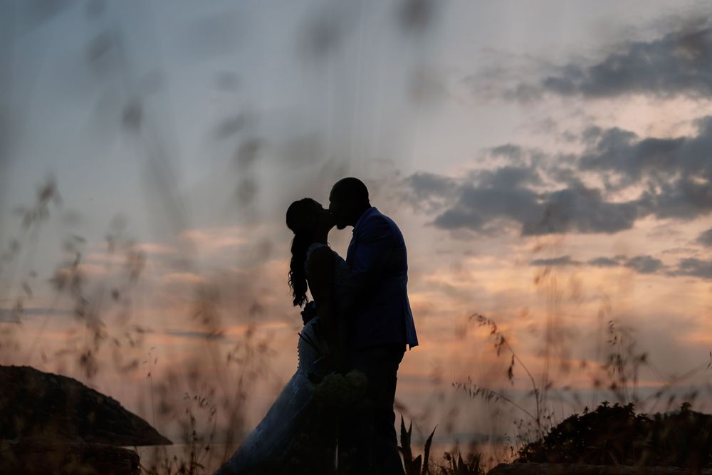 A beautiful couple shares a romantic kiss in the grass at sunset on their wedding day.