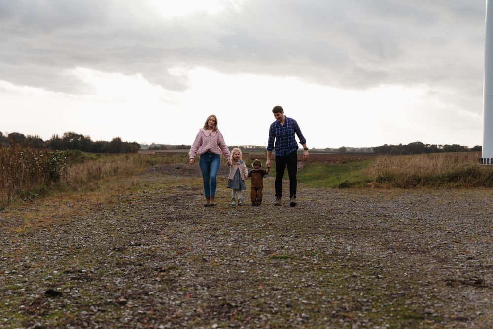 A family walks together on a gravel path under cloudy skies.