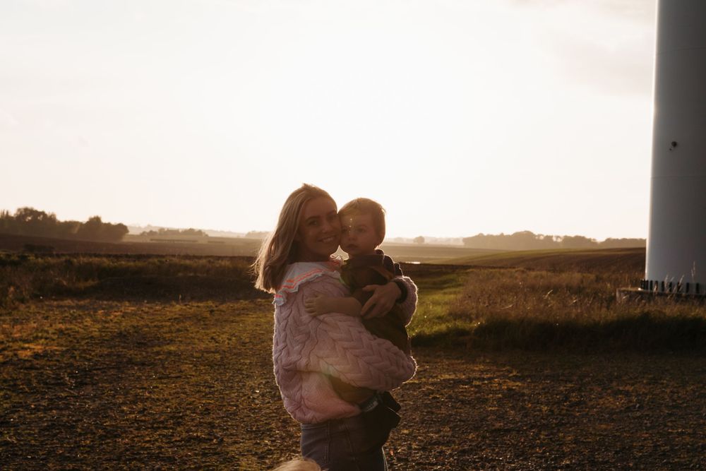 A tender sunset moment between parent and child near a wind turbine.
