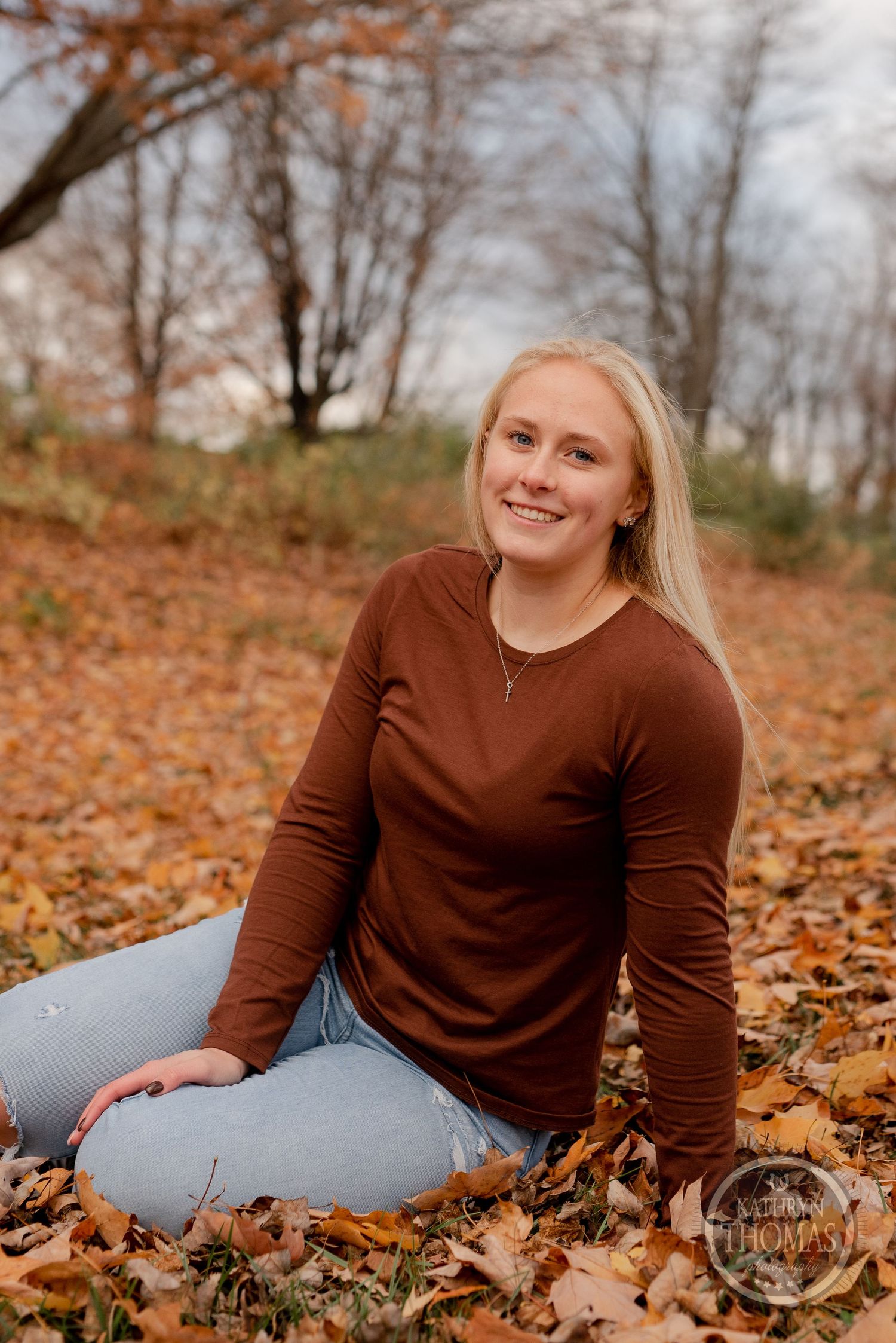 Casual outdoor portrait in brown sweater sitting among fallen autumn leaves.