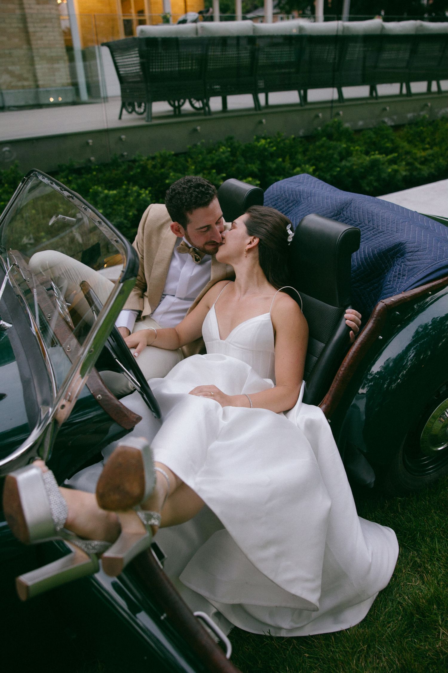 Newlyweds share intimate moment in vintage convertible car.