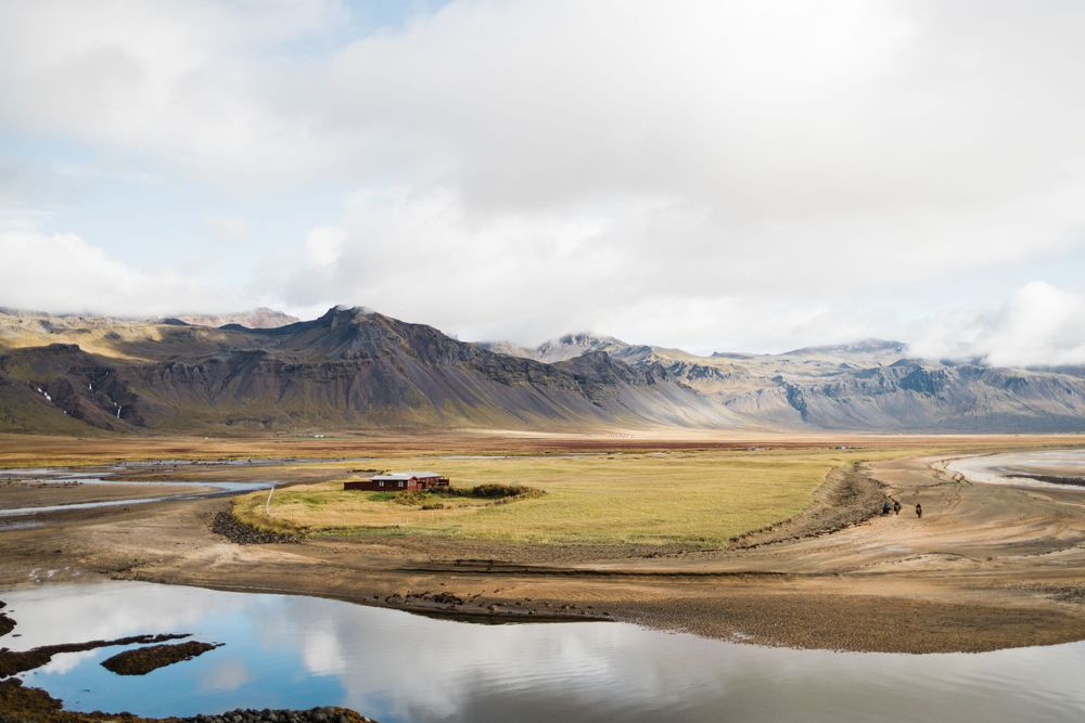 Dramatic landscape of mountains and winding river in Iceland with cloudy sky overhead.